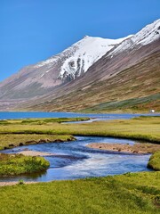 Fototapeta premium Snow-capped mountain peaks, green meadows and blue river surface in Iceland