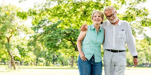 Elderly couple walking in a park, smiling and embracing. The elderly couple enjoys a sunny day, surrounded by trees, sharing a joyful moment outdoors. Happy elderly couple walking in the park.