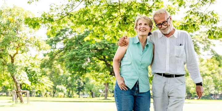 Elderly couple walking in a park, smiling and embracing. The elderly couple enjoys a sunny day, surrounded by trees, sharing a joyful moment outdoors. Happy elderly couple walking in the park.
