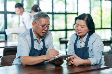 Elderly asian couple wearing aprons sitting in cafe discussing restaurant management and financial...