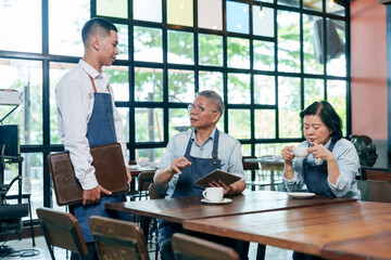 Elderly asian man restaurant owner wearing apron explaining service detail young waiter while woman...