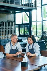 Elderly asian couple wearing aprons sitting together at wooden table discussing restaurant income...