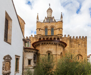 A historic stone church tower with a tiled dome and spire rises above lush green trees