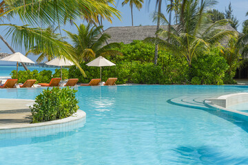 Relaxing beach resort pool leisure sun chairs beds umbrella palm trees sunny tropical weather. Summer tourism tranquil lifestyle vacation background luxury holiday destination. Tranquil Maldives scene