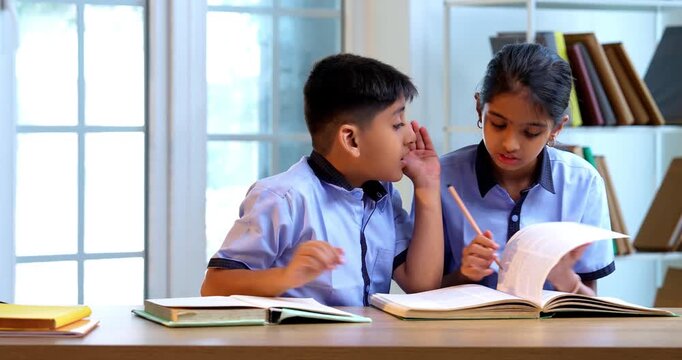 Indian School Kids Sharing Gossip with Friend in a Classroom While Wearing School Uniforms, Whispering Secret Conversations and Laughing Quietly During Leisure Moment Between Study Sessions in school