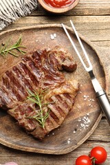 Delicious grilled beef steak with rosemary, spices and carving fork on wooden table, flat lay