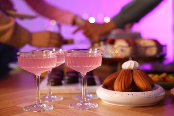 Glasses of cocktails and people with delicious desserts at buffet table, selective focus