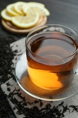 Aromatic black tea in glass cup, dried leaves and lemon on table, closeup