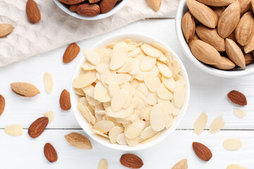Fresh almond flakes and whole nuts on white wooden table, flat lay