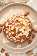 Tasty roll bun with almond flakes and nuts on wooden table, flat lay