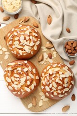 Tasty roll buns with almond flakes and nuts on white wooden table, flat lay