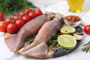 Fresh raw squids, tomatoes, lime slices and spices on white marble table, closeup