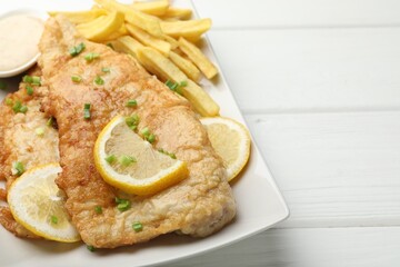 British Traditional Fish and chips with sauce, lemon and green onion on white wooden table, closeup