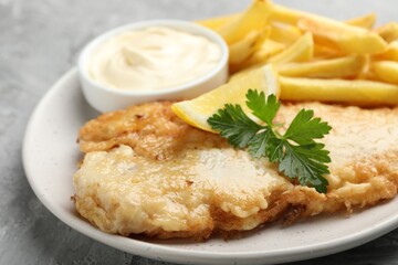 British Traditional Fish and chips with sauce, lemon and parsley on gray table, closeup