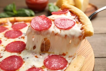 Taking piece of delicious pepperoni pizza at wooden table, closeup