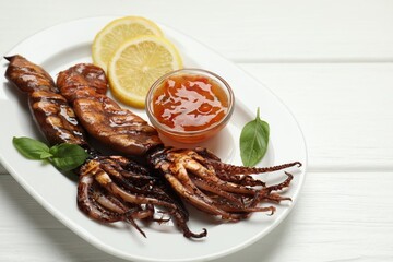 Tasty cooked squids served with lemon, sauce and basil on white wooden table, closeup. Space for text
