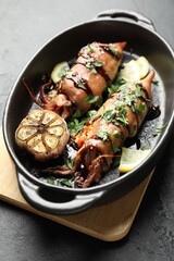 Tasty cooked squids with sauce and garlic in dish on black table, closeup