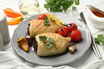 Pieces of tasty grilled squid stuffed with mushrooms, parsley and tomatoes on white wooden table, closeup