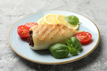 Piece of tasty grilled squid stuffed with mushrooms, basil, tomatoes and lemon on grey textured table, closeup