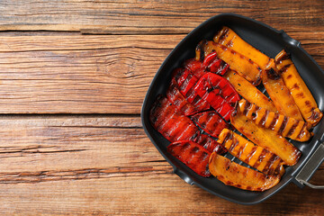 Delicious grilled peppers in pan on wooden table, top view. Space for text