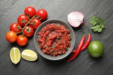 Delicious salsa sauce in bowl and ingredients on dark grey table, flat lay
