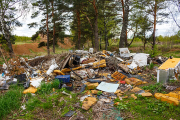 Huge pile of trash and discarded items polluting a natural forest landscape. Environmental blight and illegal dumping near trees