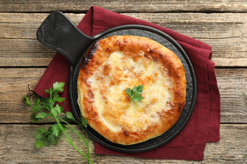 Delicious Megrelian khachapuri with parsley on wooden table, flat lay