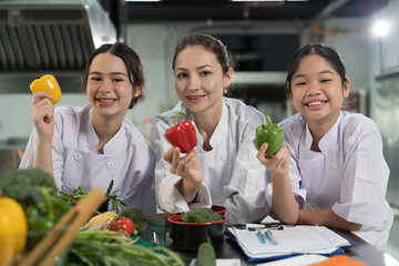 Cooking, Kitchen. Group of young female chef wearing white apron and holding vegetables during...