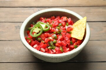 Tasty salsa with nacho chip on wooden table, closeup
