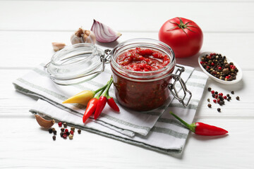 Tasty salsa sauce in jar and ingredients on white wooden table