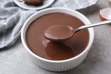 Taking raw chocolate dough from bowl with spoon on grey table, closeup