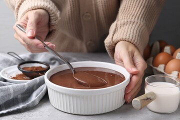 Woman with raw chocolate dough in bowl at grey table, closeup