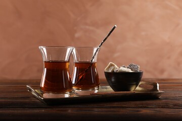 Tasty Turkish tea in glass cups and sweets on wooden table against brown background, closeup