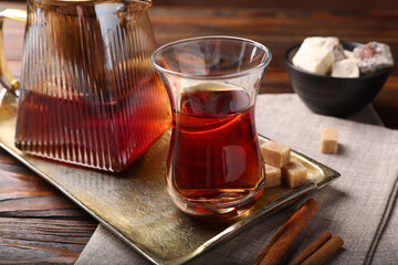 Tasty Turkish tea in glass cup, brown sugar, cinnamon, sweets and teapot on wooden table, closeup