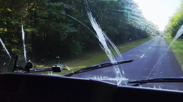 Clear view of winding road and green scenery with dirty windshield during a sunny drive