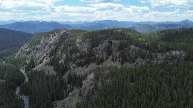 Mountain scenery along the Beartooth Highway in Wyoming. Closeup flying shot pushes in over a valley towards a rugged mountain peak in the distance.