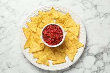 Tasty salsa in bowl and nachos on white marble table, top view