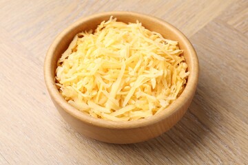 Grated cheese in bowl on wooden table, closeup
