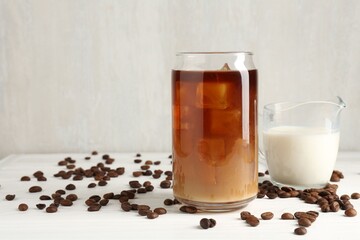 Tasty iced coffee with milk and beans on white wooden table. Space for text