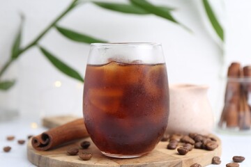 Tasty iced coffee in glass and beans on white table, closeup