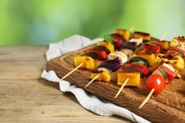 Skewers with tasty grilled vegetables on wooden table against blurred background, closeup. Space for text
