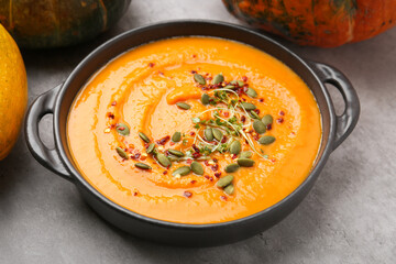 Delicious pumpkin soup in bowl and vegetables on grey table, closeup