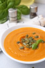 Delicious pumpkin soup with seeds and basil in bowl on light table, closeup