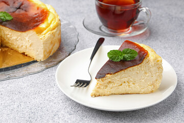 Piece of delicious Basque cheesecake with mint and tea on light grey table, closeup