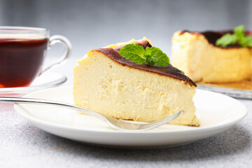 Piece of delicious Basque cheesecake with mint and tea on light grey table, closeup