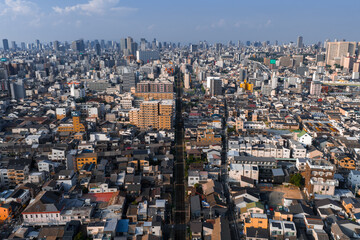 Fototapeta premium Aerial view of Osaka, Japan, with low and mid rise districts, a straight railway cutting center, and modern skyscrapers in soft daytime light under clear conditions.