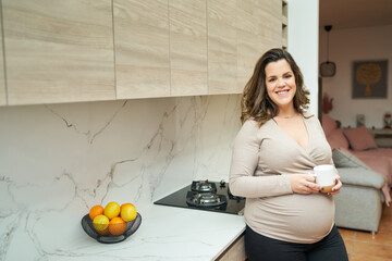 Pregnant woman holding mug in home kitchen