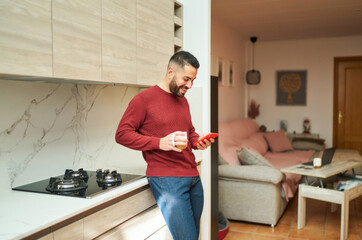 Man drinking coffee and using smartphone in kitchen