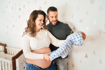Expectant couple preparing nursery, holding baby clothes