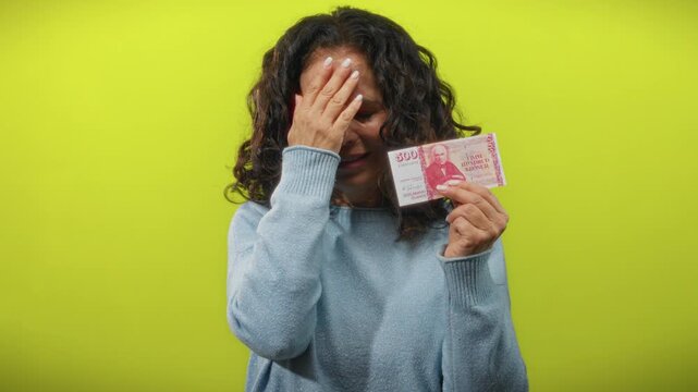Woman holding icelandic krona appears worried against a bright yellow background.